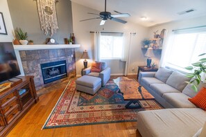 A living room with a fireplace, a ceiling fan, and a large window.