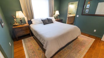 Quarto bem arrumado com cama, mesas de cabeceira, espelho e janela com cortinas.