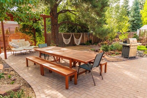 An outdoor patio with a wooden table and benches, surrounded by a wooden fence and trees.