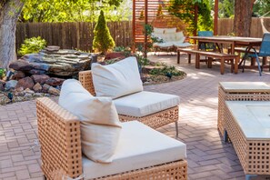 Un patio amueblado con mobiliario de mimbre, que incluye un sofá y una mesa, rodeado de piso de ladrillo y cerca de madera.