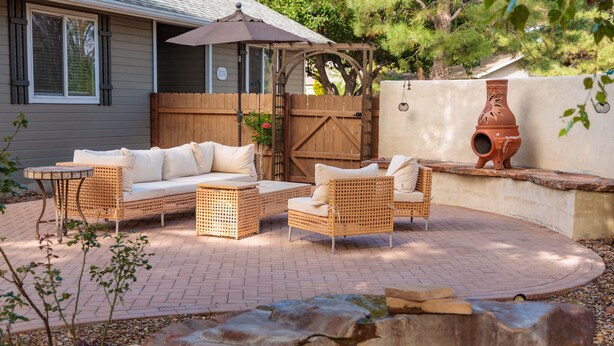 An outdoor patio with wicker furniture, a wooden fence, and a potted plant.