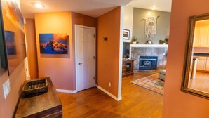 A hallway leading to a living room with a fireplace, wooden flooring, and a door with a picture on the wall.