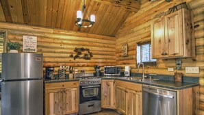 A log cabin kitchen with a stainless steel refrigerator, stove, oven, and dishwasher. - Cozy and Rustic "Bear Themed" Cabin~private pond and 7 miles to YNP entrance! (West Yellowstone)