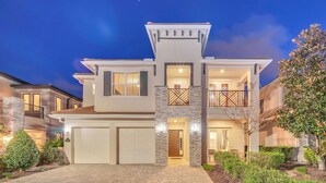 A modern two-story house with a garage, a balcony, and a well-lit entrance. - Paradise at Bear's Den | 6-Bed Villa w/ Loft, Games Room, and Private Pool (Kissimmee)