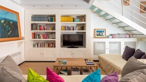 Un salon moderne avec une bibliothèque, un téléviseur à écran plat, une table basse et un escalier.