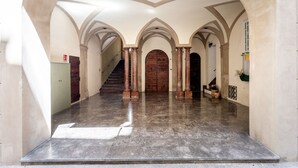 Un vaste hall d’entrée avec un sol en marbre poli, un escalier et une porte en bois au fond.