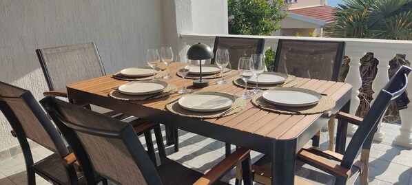 A wooden table set with plates, glasses, and a lamp on a balcony with chairs.