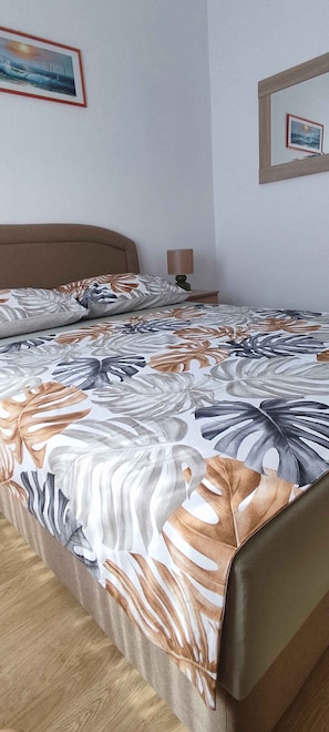 A bed with a floral bedspread, a bedside table with a lamp, and a framed picture on the wall. - Holiday apartment with air conditioning and sea view (Vir)