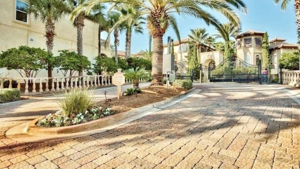 Un vialetto lastricato fiancheggiato da palme e un cancello che introduce a un edificio in stile mediterraneo.