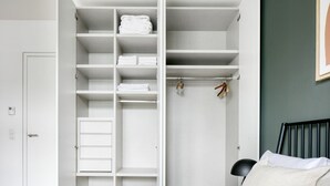Een slaapkamer met een bed, een witte kledingkast met meerdere planken en een nachtkastje.