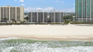 Un hotel frente a la playa con varios edificios altos, una playa de arena y olas rompiendo en la orilla.