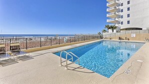 Una piscina con una escalera metálica, vista a la playa y un edificio alto con balcones.