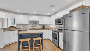 Una cocina moderna con armarios blancos, un refrigerador de acero inoxidable, un horno empotrado y una isla de madera con taburetes.