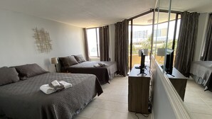 Een hotelkamer met twee bedden, een bureau met een computer en een groot raam met gordijnen.