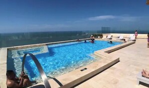 Ein Pool im Freien mit freiem Blick auf den Ozean, Liegestühle und eine Person, die eine Poolleiter benutzt.
