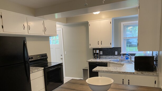 A modern kitchen with white cabinets, a black refrigerator, a wooden table, and a window with blinds. - Lorie house Avon ohio (Avon)