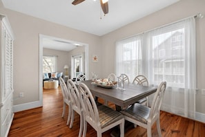 A dining area with a wooden table, white chairs, and a view of the outdoors through large windows.