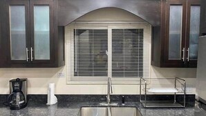 Een keuken met donkere houten kasten, een roestvrijstalen spoelbak, een koffiezetapparaat en een raam met jaloezieën.
