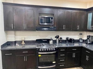 A kitchen with dark cabinets, a microwave, a stove, an oven, and various appliances like a coffee maker and a blender.