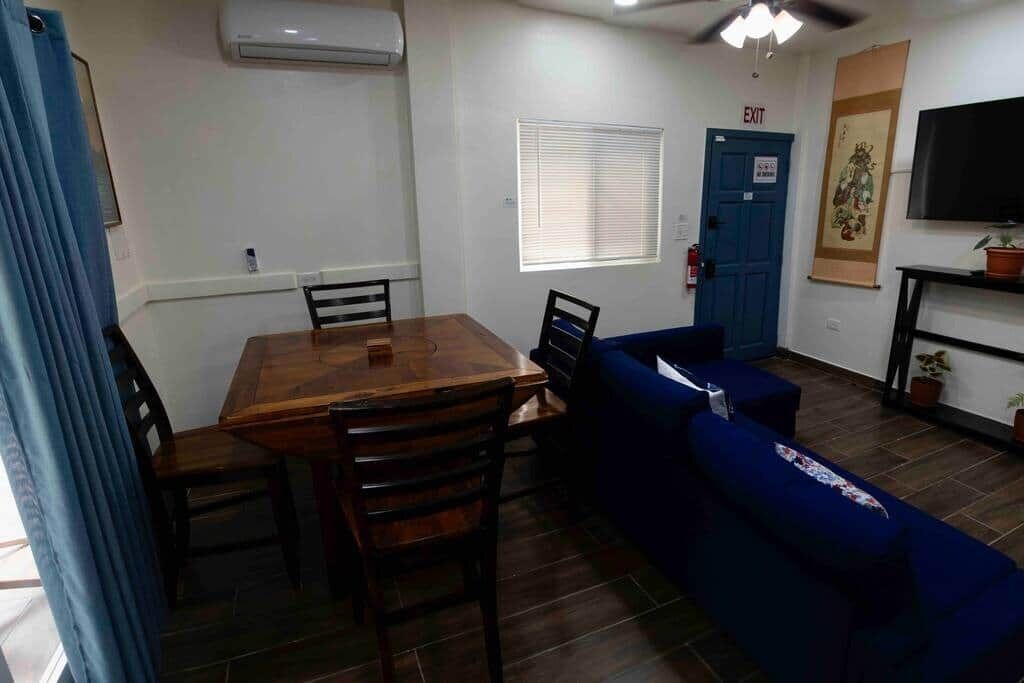 A room with a wooden dining table, blue sofa, and a TV on the wall.