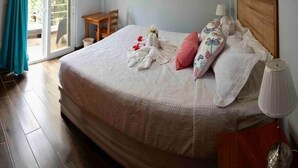 Een slaapkamer met een bed, een aan de muur bevestigde televisie, een tafel en stoel, en een schuifdeur naar buiten.