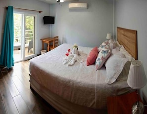 A bedroom with a bed, a TV mounted on the wall, a table and chair, and a sliding door to the outside. - MeMe’s Place Villa #1 (Belize City)