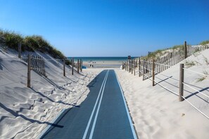Ein Weg, der zu einem Sandstrand führt, mit blauem Himmel.
