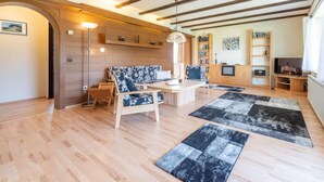 Een ruime woonkamer met houten vloeren, een zithoek, een salontafel, een boekenkast en een televisie.