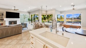 Uma cozinha moderna com uma ilha grande, uma área de jantar com mesa de bilhar e uma sala de estar com lareira.