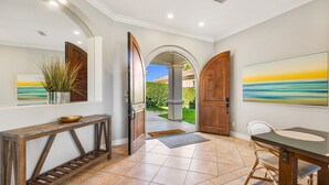 Um corredor com um aparador de madeira, uma cadeira de vime e uma pintura do pôr do sol.