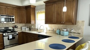 A kitchen with wooden cabinets, a stainless steel stove, a microwave, and a blue coffee maker.