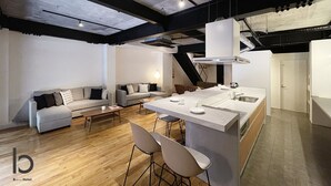 A modern kitchen with a central island, bar stools, and a dining area with a sofa and coffee table. - bHotel Kaniwasou (Hatsukaichi)