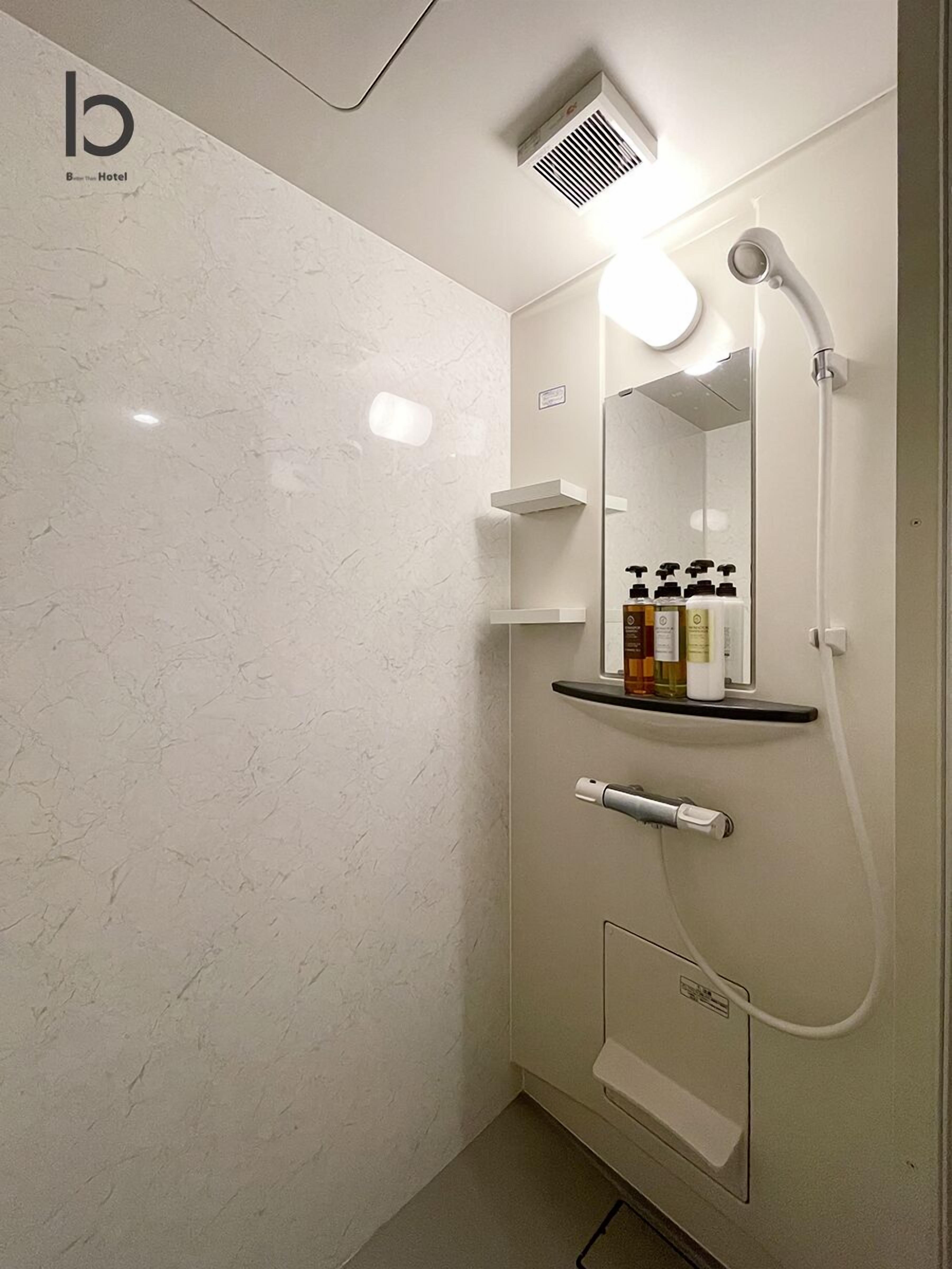 A modern bathroom with a marble wall, a built-in shelf with toiletries, a handheld showerhead, and a wall-mounted mirror.