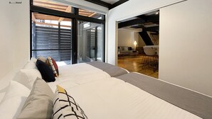 A modern hotel room with a large bed, a sofa, and a dining area visible through a glass door. - bHotel Kaniwasou (Hatsukaichi)