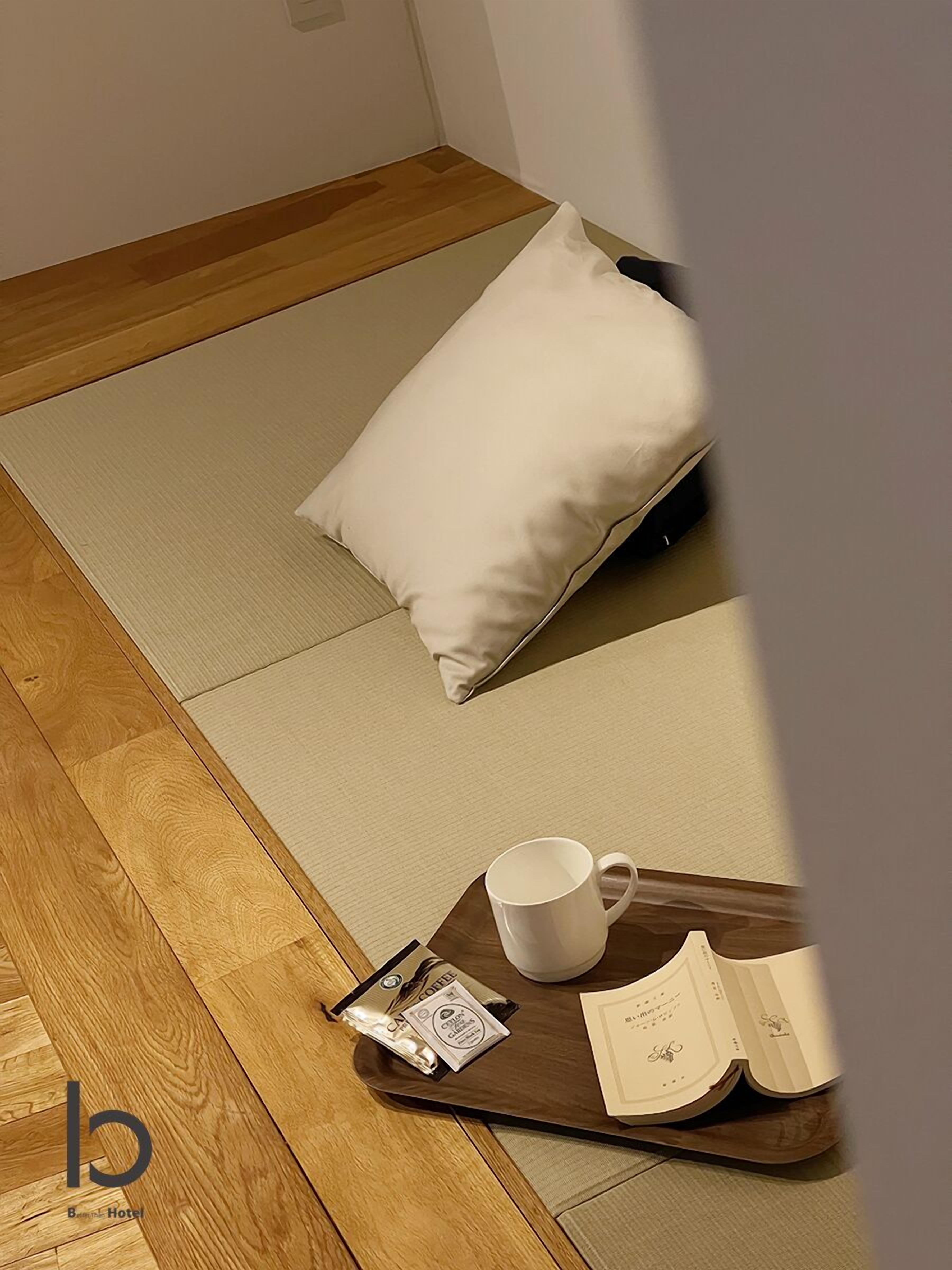 A tatami mat room with a pillow, a tray with a coffee packet, a mug, and an open menu.