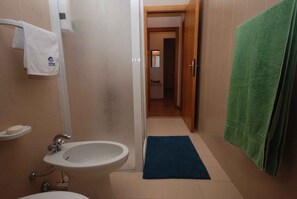 Un baño con un bidé, un lavabo, un perchero y una toalla verde colgada en la pared.