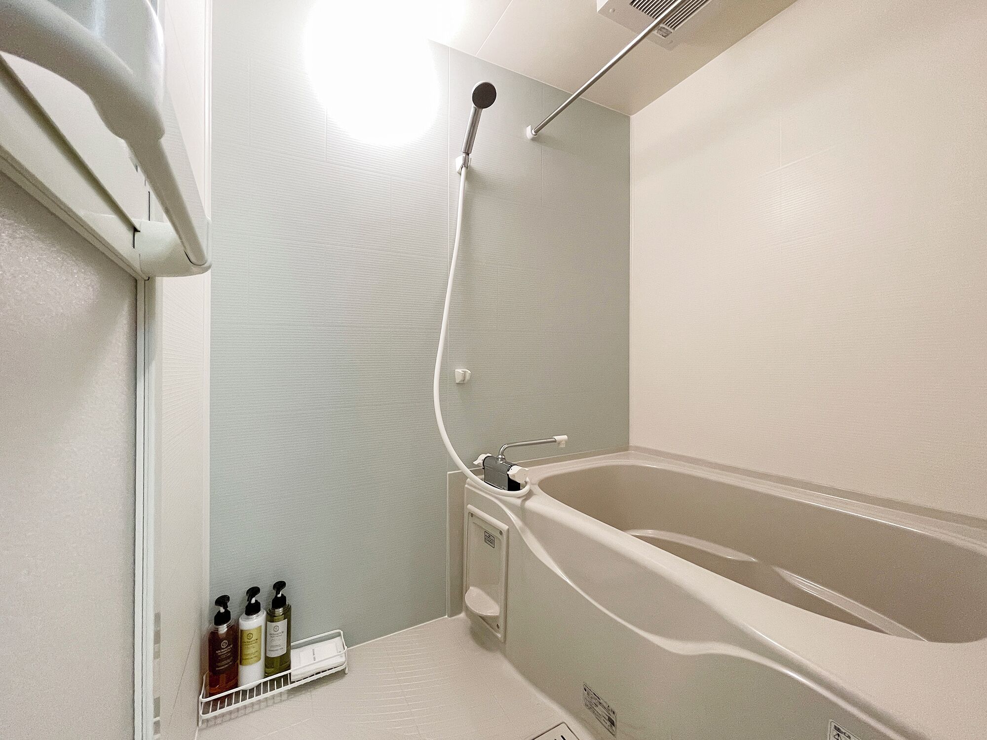 A bathroom with a bathtub, a showerhead, and a shelf with toiletries.
