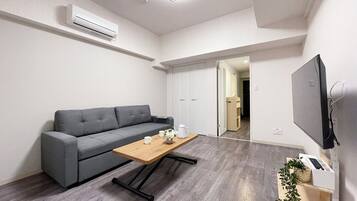 Ett modernt vardagsrum med en grå soffa, ett soffbord i trä och en platt-TV som är monterad på väggen.