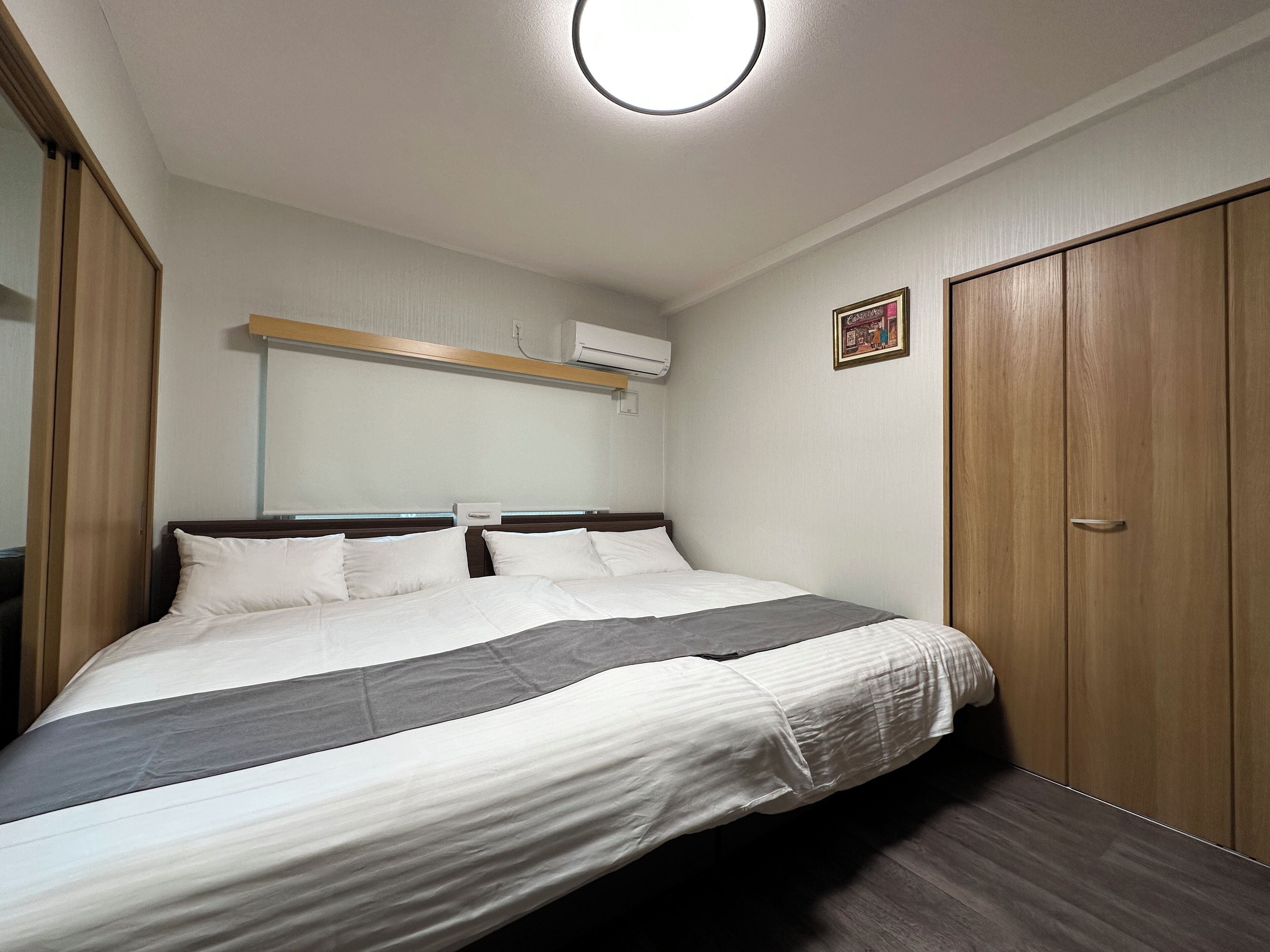 A bedroom with a bed, wooden wardrobe, and an air conditioning unit on the wall.