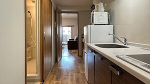 A modern kitchen with wooden flooring, a built-in oven, a microwave, and a sink. - CasaEn (Hiroshima)