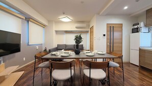 A modern dining area with a wooden table, four chairs, and a vase of flowers. - CasaEn (Hiroshima)