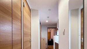 A hallway with wooden flooring, a mirror on the right, and a door on the left. - CasaEn (Hiroshima)