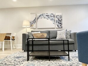 A modern living room with a grey sofa, patterned cushions, a black coffee table, and a decorative wall piece.