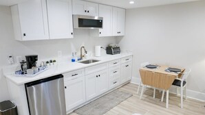 A modern kitchen with white cabinets, a stainless steel dishwasher, a microwave, and a small dining area with a table and chairs. - Beautiful & Modern-near Subway Parking! (Washington)