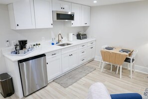 A modern kitchen with white cabinets, a stainless steel dishwasher, a microwave, and a wooden dining table with chairs.