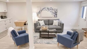 A living room with a grey sofa, two blue armchairs, a coffee table, and a modern abstract painting on the wall. - Beautiful & Modern-near Subway Parking! (Washington)