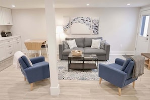 Uma sala de estar moderna com um sofá cinza, duas poltronas azuis, uma mesa de centro e um objeto decorativo na parede.