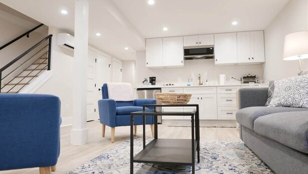 A modern living room with a sofa, a blue armchair, a small table, and a kitchen area with white cabinets and a microwave. - Beautiful & Modern-near Subway Parking! (Washington)