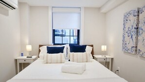 A hotel room with a large bed, two bedside tables with lamps, a window with blinds, and a decorative wall panel. - Beautiful & Modern-near Subway Parking! (Washington)