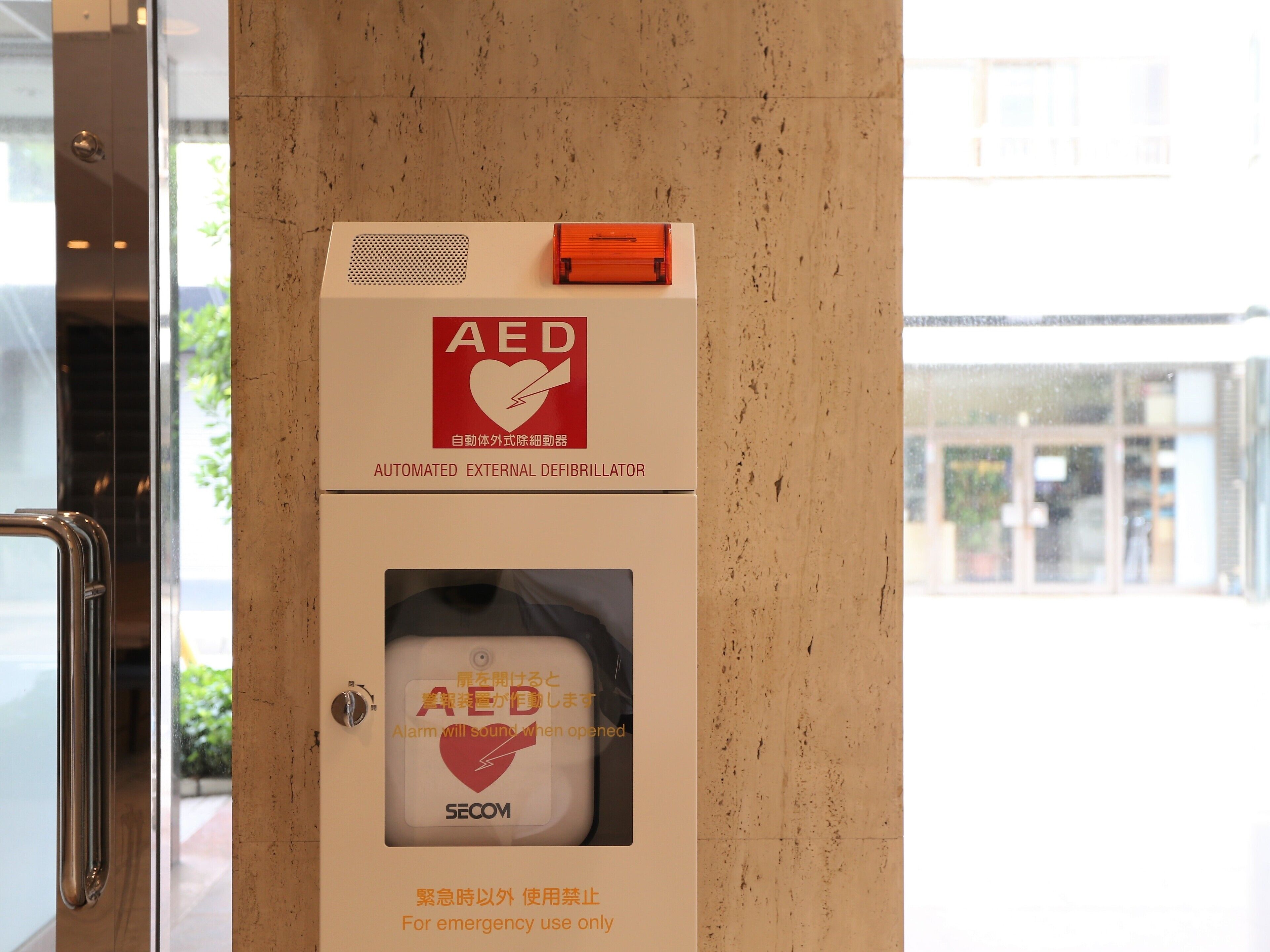 Kit di emergenza con defibrillatore automatico esterno montato su una parete, con segnale di avvertimento e maniglia.
